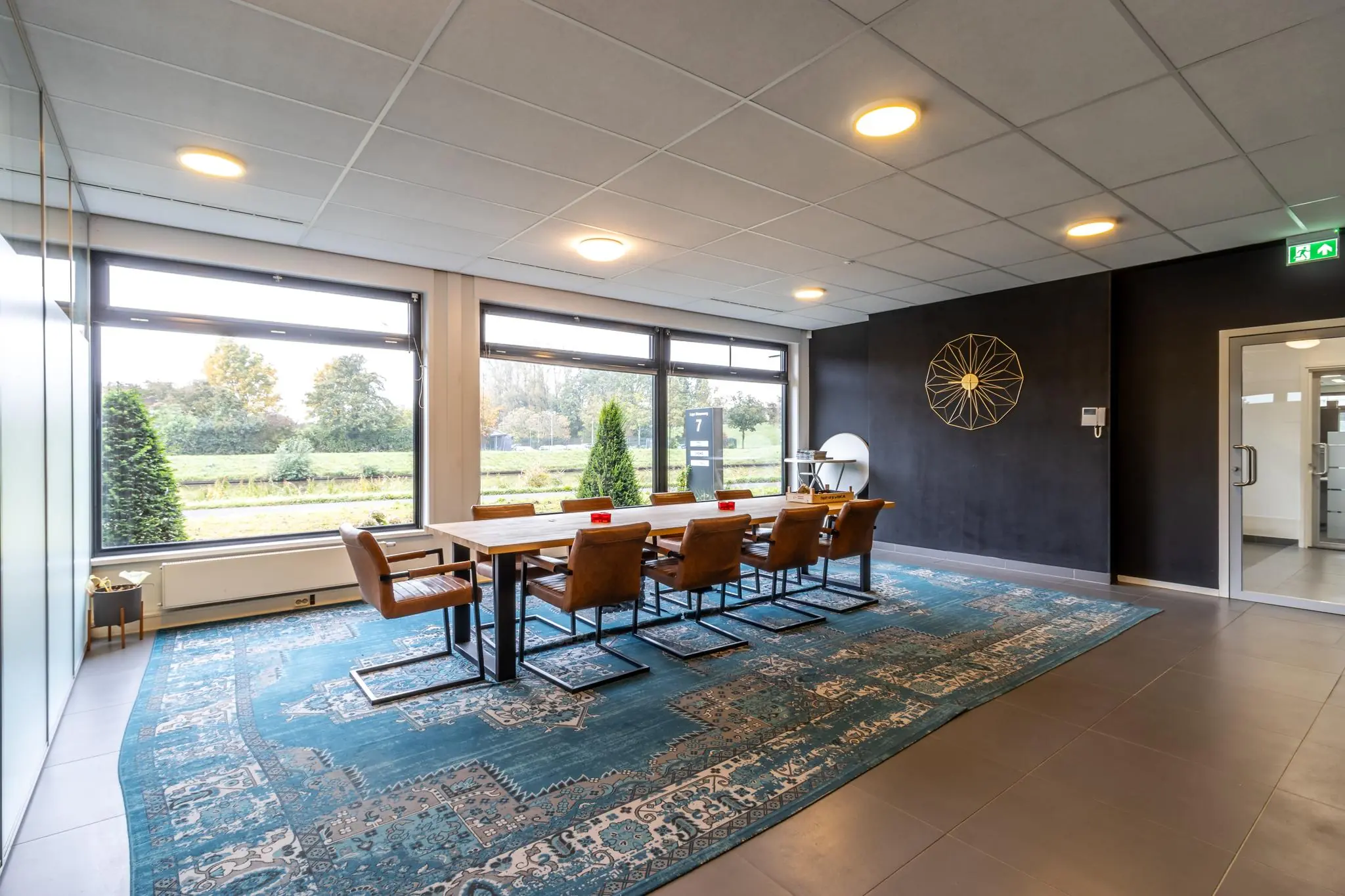 Vergaderruimte aan de Lage Biezenweg met een lange houten tafel, leren stoelen, groot vloerkleed en uitzicht op groen landschap.